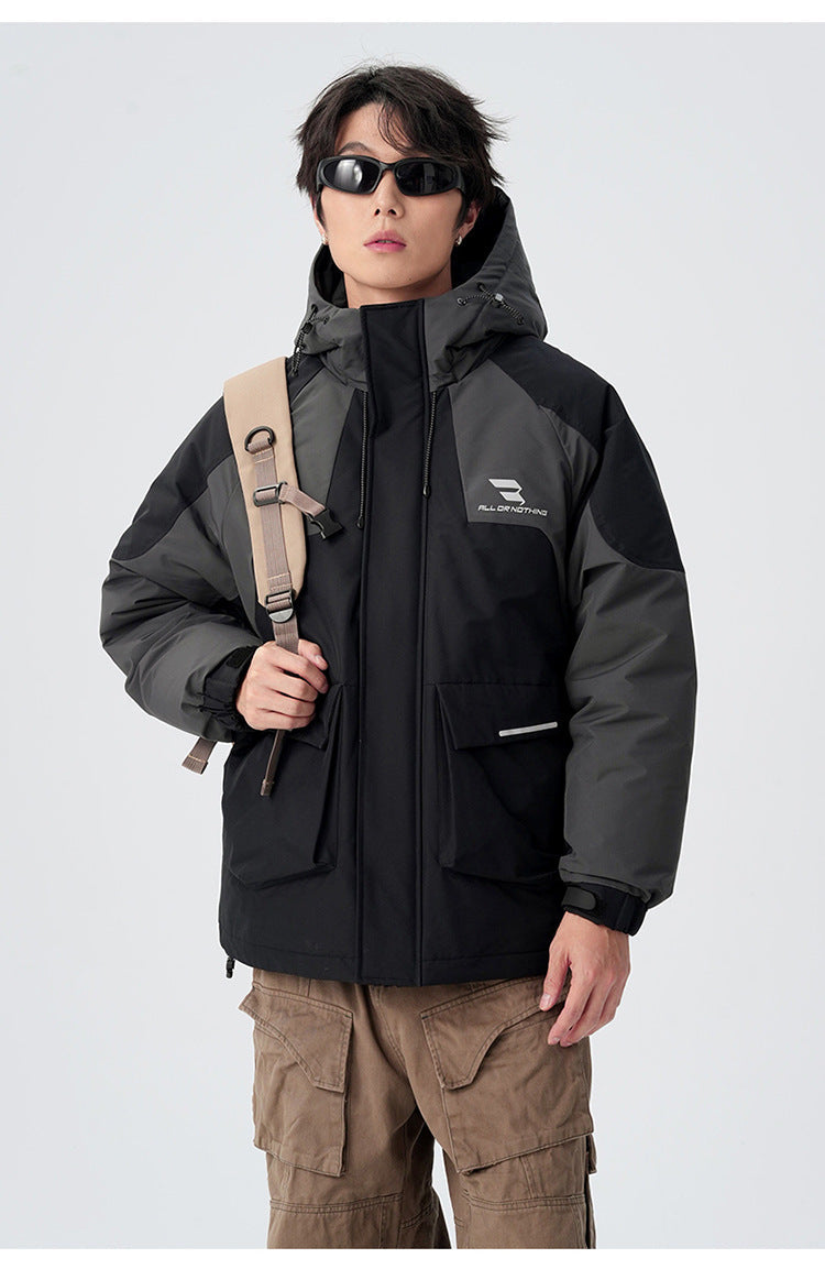 A man wearing black sunglasses and gray/black All Drifting technical jacket stands with shoulder bag against white backdrop