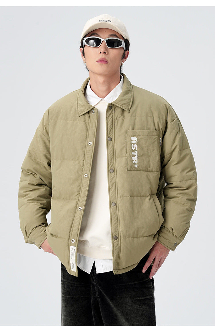 Model in olive green ASTROSMASH puffer jacket with cream cap, white shirt, oval sunglasses and black pants against neutral backdrop