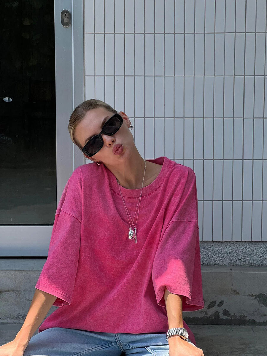 Person wearing a pink oversized shirt sitting against a tiled wall.