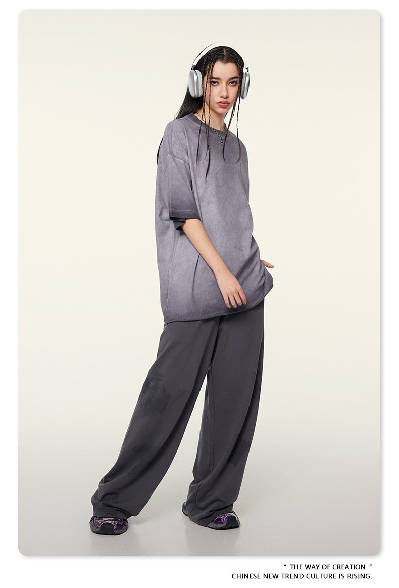 Model wearing gray oversized t-shirt and dark pants with silver headphones against cream background