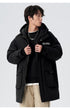 A man adjusting black Be_Born parka showing chest logo detail and silver necklace against white background