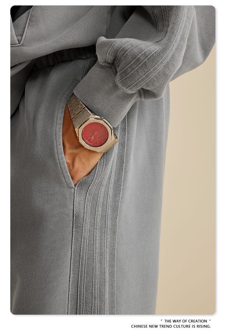 Close-up of silver watch with red face detail visible with hand in grey sweatpants pocket