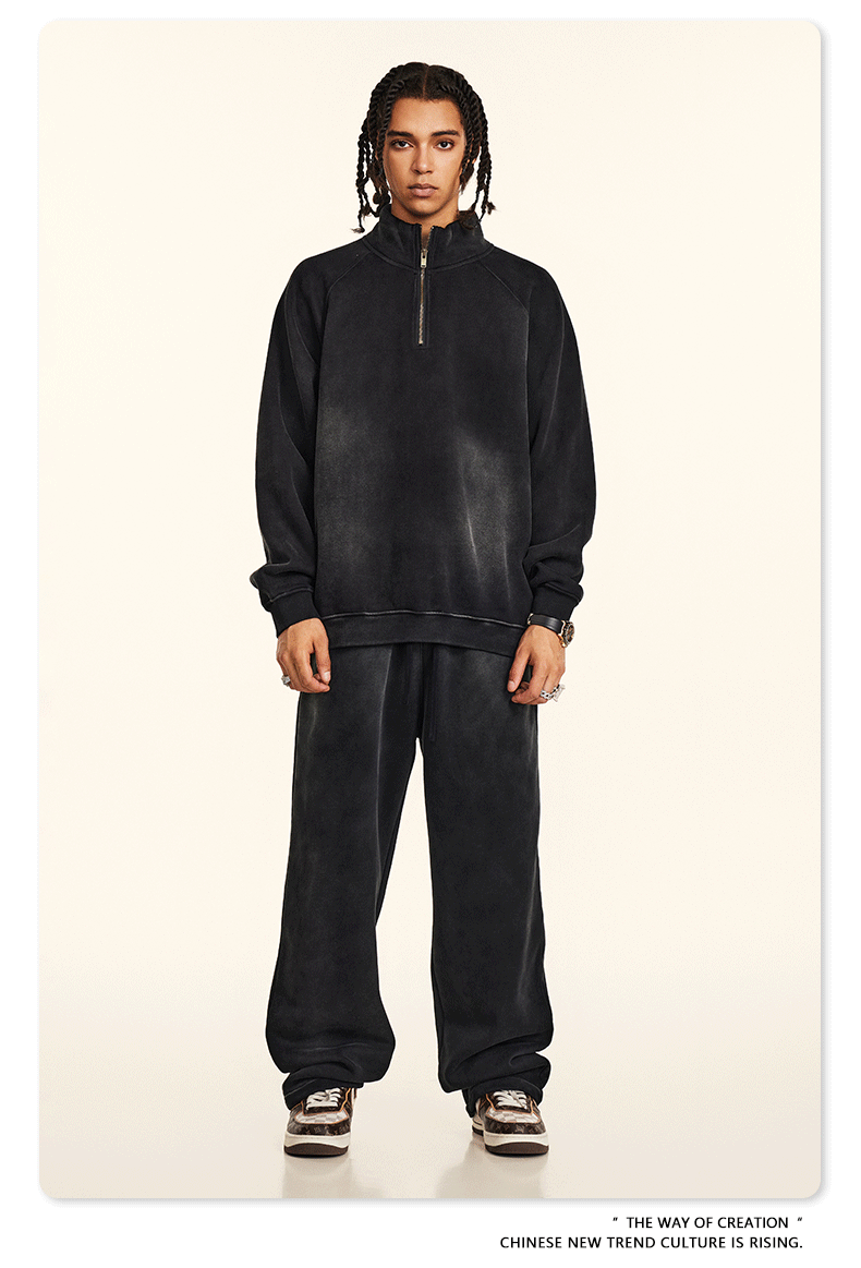 Model with braided hair wearing black quarter-zip sweatshirt and matching wide-leg pants against cream background