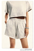 Side view of beige crop top and shorts set with elastic waistband and silver bracelet accessory