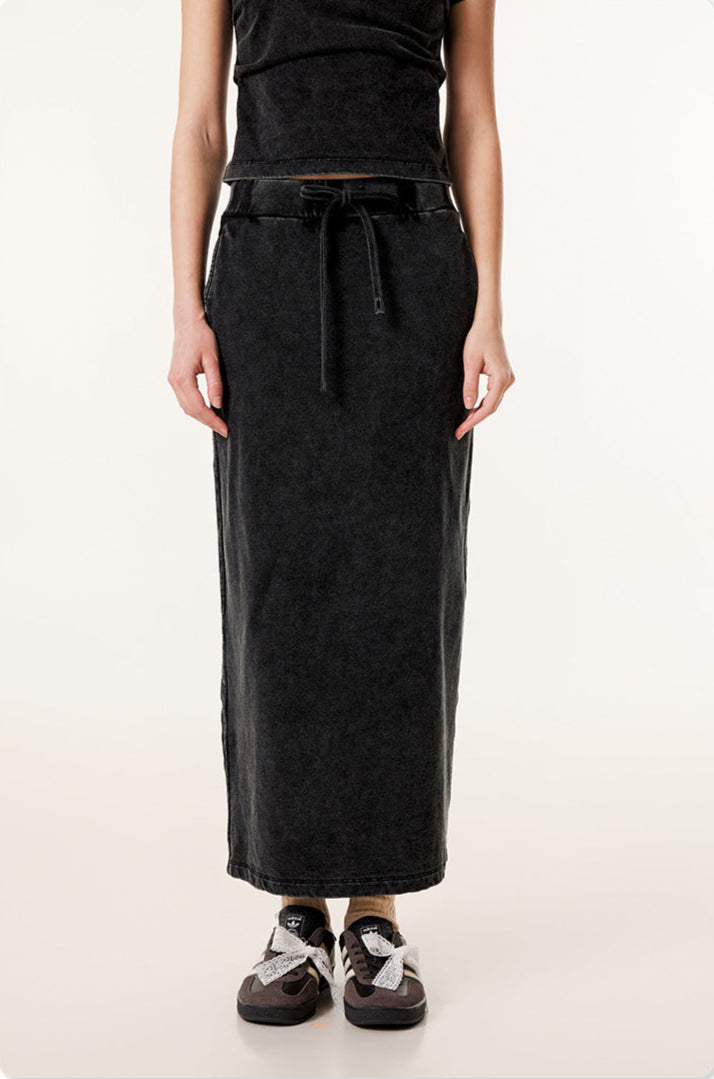 Long black denim skirt with drawstring waist and side pockets, paired with gray and black sneakers with white laces