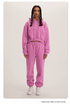 Pink Sweatshirt and Joggers Set – Model wears a vibrant pink cropped hoodie and matching sweatpants with white sneakers