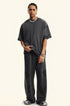 Model in charcoal grey matching set with hand gesture showing oversized t-shirt fit. Features silver chain necklace, watch and chunky black footwear