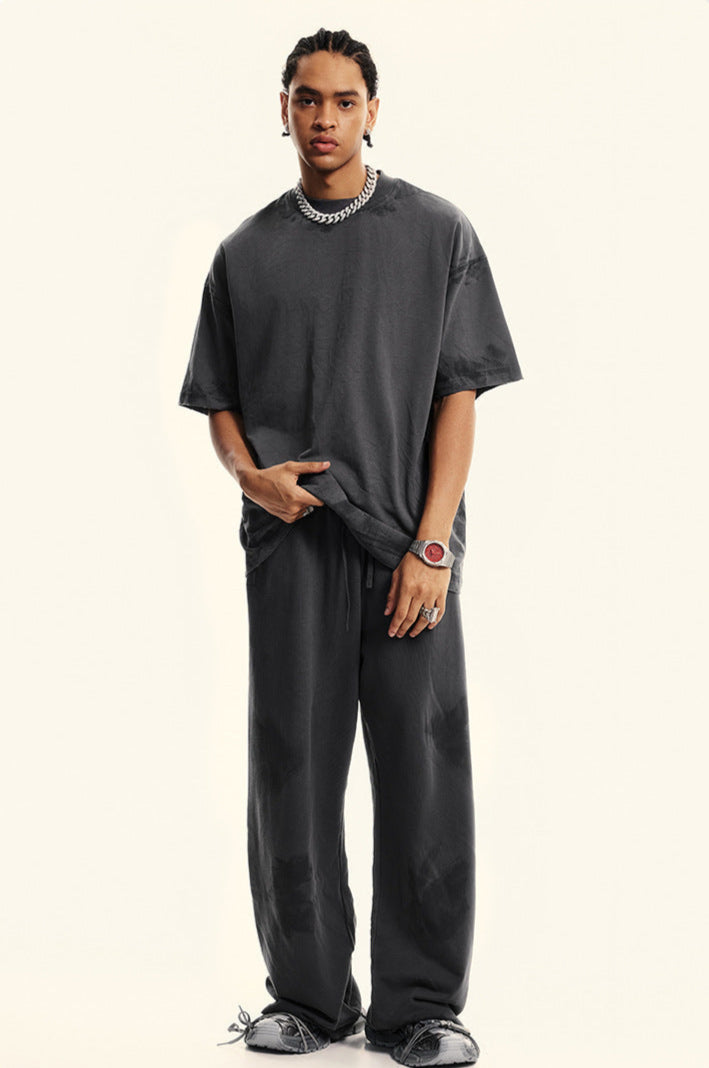 Model in charcoal grey matching set with hand gesture showing oversized t-shirt fit. Features silver chain necklace, watch and chunky black footwear