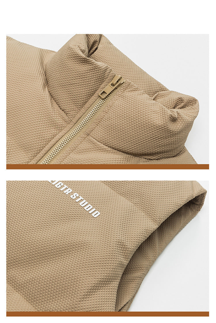 Close-up of tan puffer vest collar showing quilted texture and metal zipper details against white background