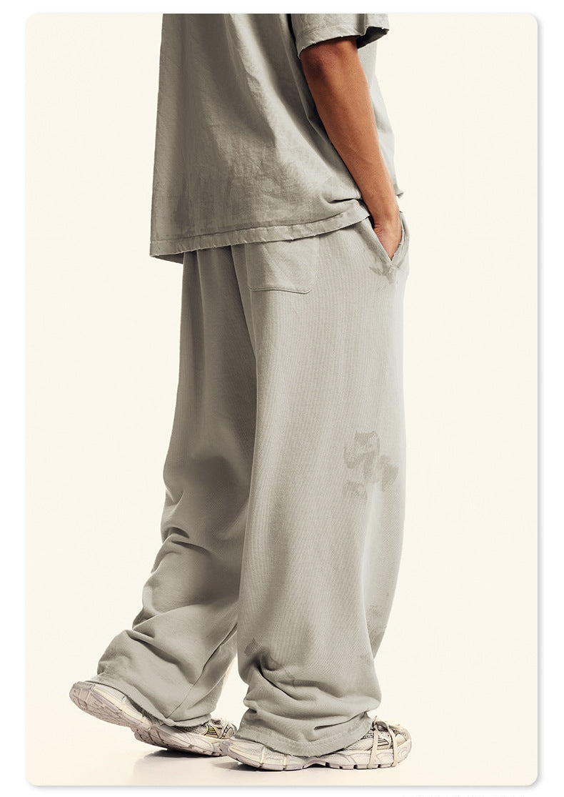 Close-up of cream Backstairs sweatpants leg showing distressed paint effect pattern and white athletic shoe against white background