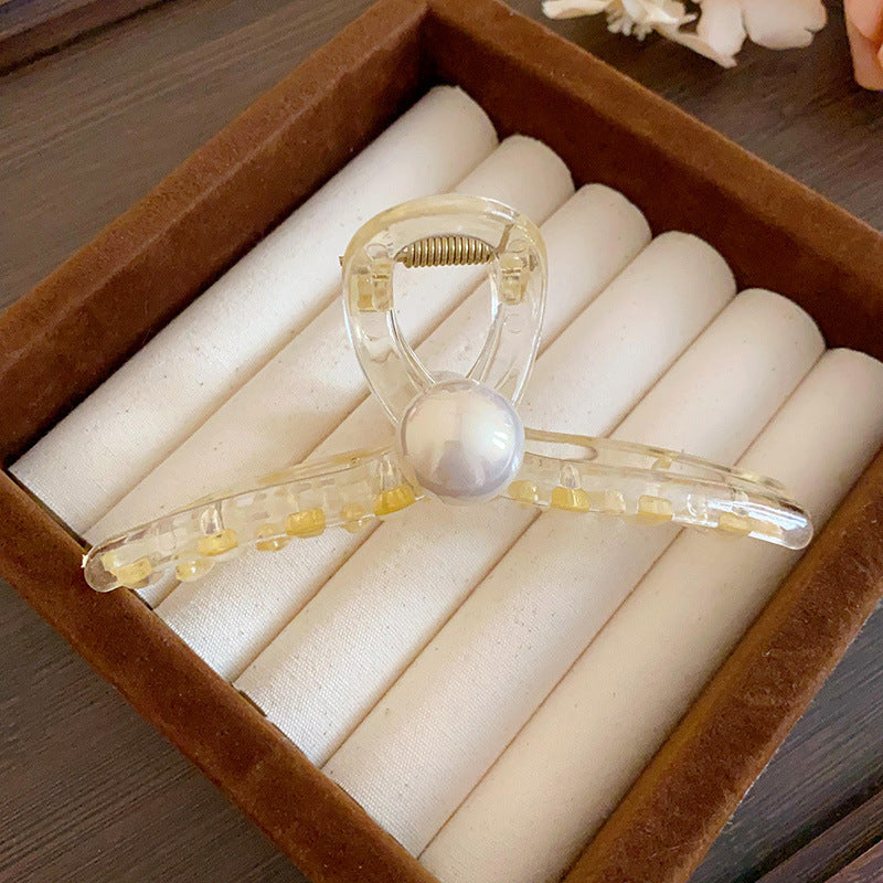 A champagne-colored pearl-accented hair claw with a transparent design, placed in a velvet jewelry box.

