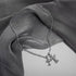 Silver gothic-style cross pendant necklace with crystal accents draped across flowing gray silk fabric