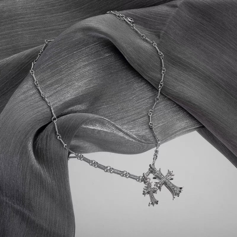 Silver gothic-style cross pendant necklace with crystal accents draped across flowing gray silk fabric