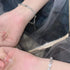 A woman is showcasing a dainty silver bracelet with alternating heart charms and crystals on her wrist against dark tulle fabric