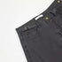 Close-up of waistband detail showing ITKN label, brass button, and adjustable side straps against white backdrop