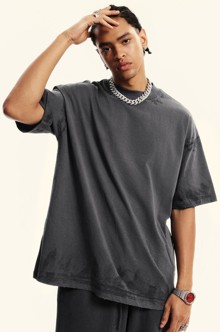 Close-up portrait of model in grey t-shirt with hand touching hair. Showcases silver chain necklace, statement watch and relaxed streetwear aesthetic