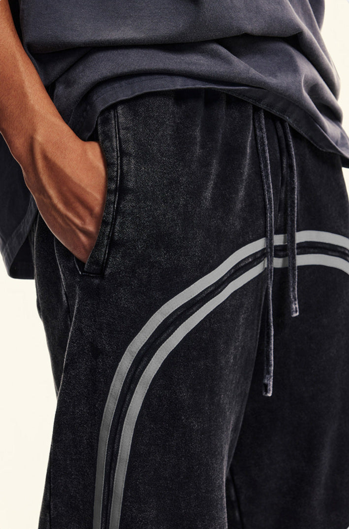 Detail shot of side pocket on black washed denim joggers with elastic waistband and gray stripe accent along sides