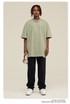 Man with short dreadlocks wearing light sage green oversized t-shirt, black sweatpants, silver chain necklace and white bracelet against neutral background