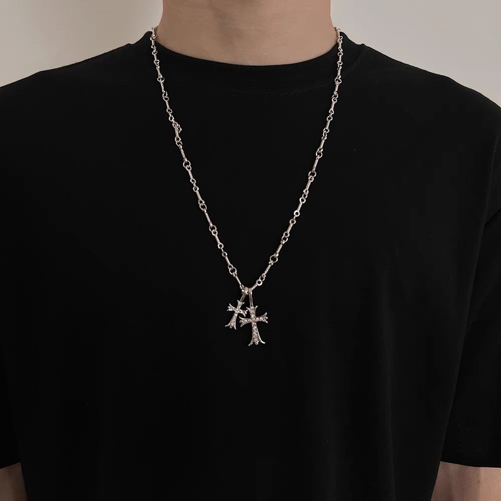 A person wearing a black t-shirt with silver chain necklace featuring two ornate cross pendants against dark background