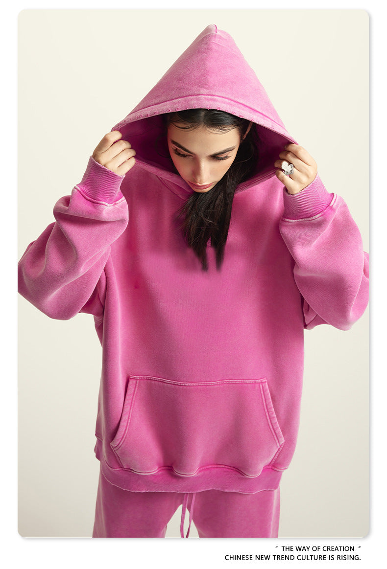 Woman adjusting hood of oversized pink hoodie sweatshirt with kangaroo pocket against neutral background