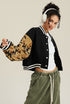 Black varsity jacket with tan camouflage sleeves, viewed from back angle, showing cropped silhouette