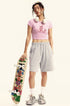 Model wearing a pink graphic crop top and gray sweat shorts, holding a skateboard with colorful artwork