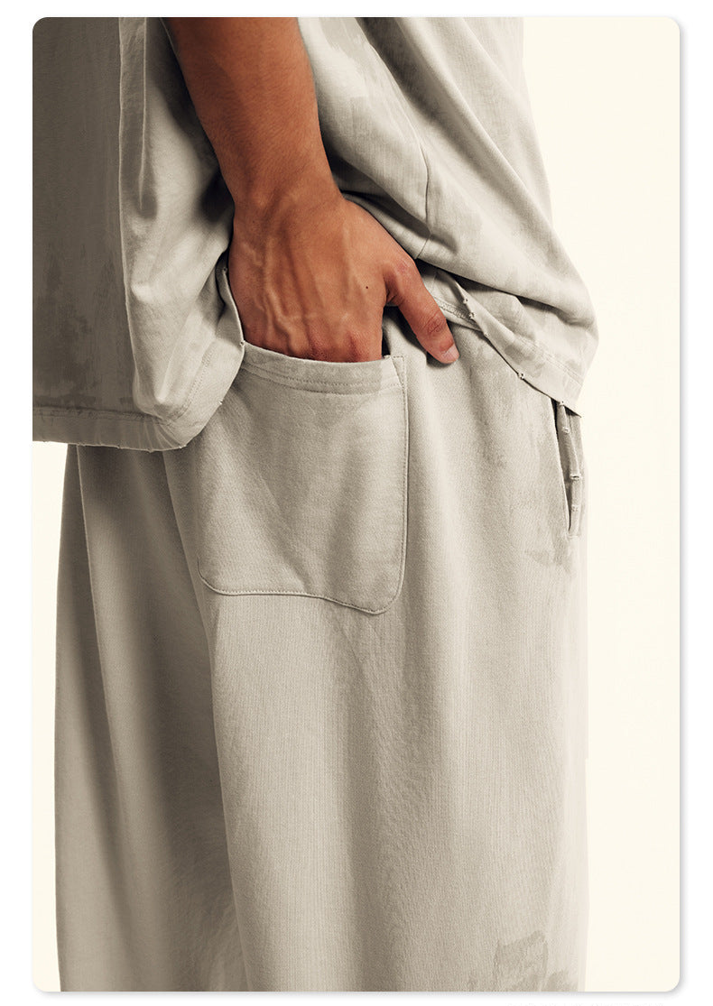 Close-up of black Backstairs sweatpants fabric showing pocket detail and distressed paint effect pattern against white background
