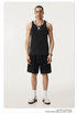 Male model in a washed black tank top and matching shorts, styled with silver jewelry, white socks, and black-striped sneakers