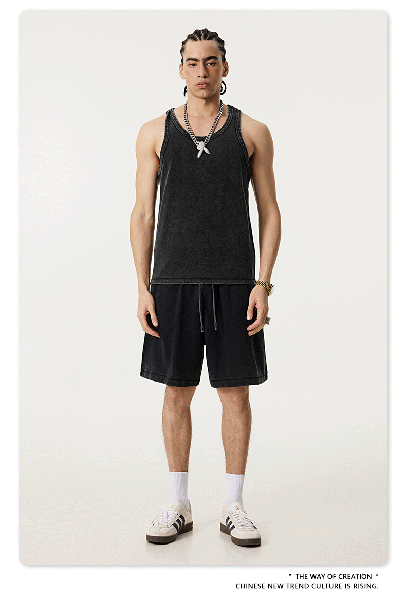 Male model in a washed black tank top and matching shorts, styled with silver jewelry, white socks, and black-striped sneakers