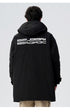 Back view of man wearing black Be_Born Beacaac parka showing white logo text and beige pants against white background