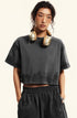 A woman wearing gold headphones poses in a dark gray cropped t-shirt and matching shorts against a white background
