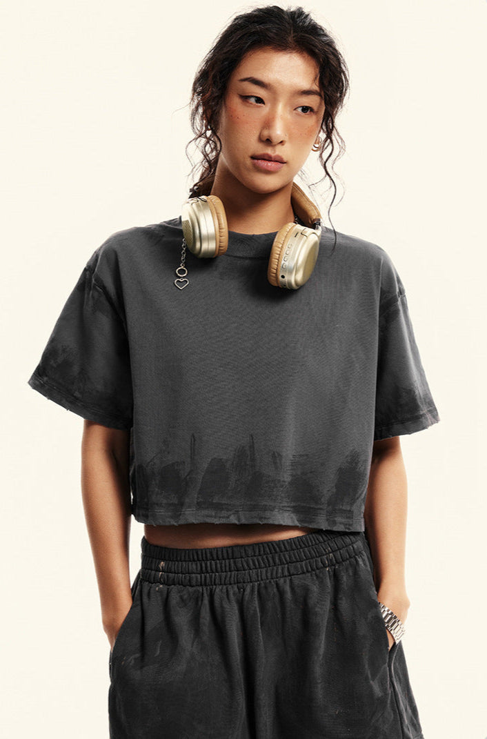 A woman wearing gold headphones poses in a dark gray cropped t-shirt and matching shorts against a white background