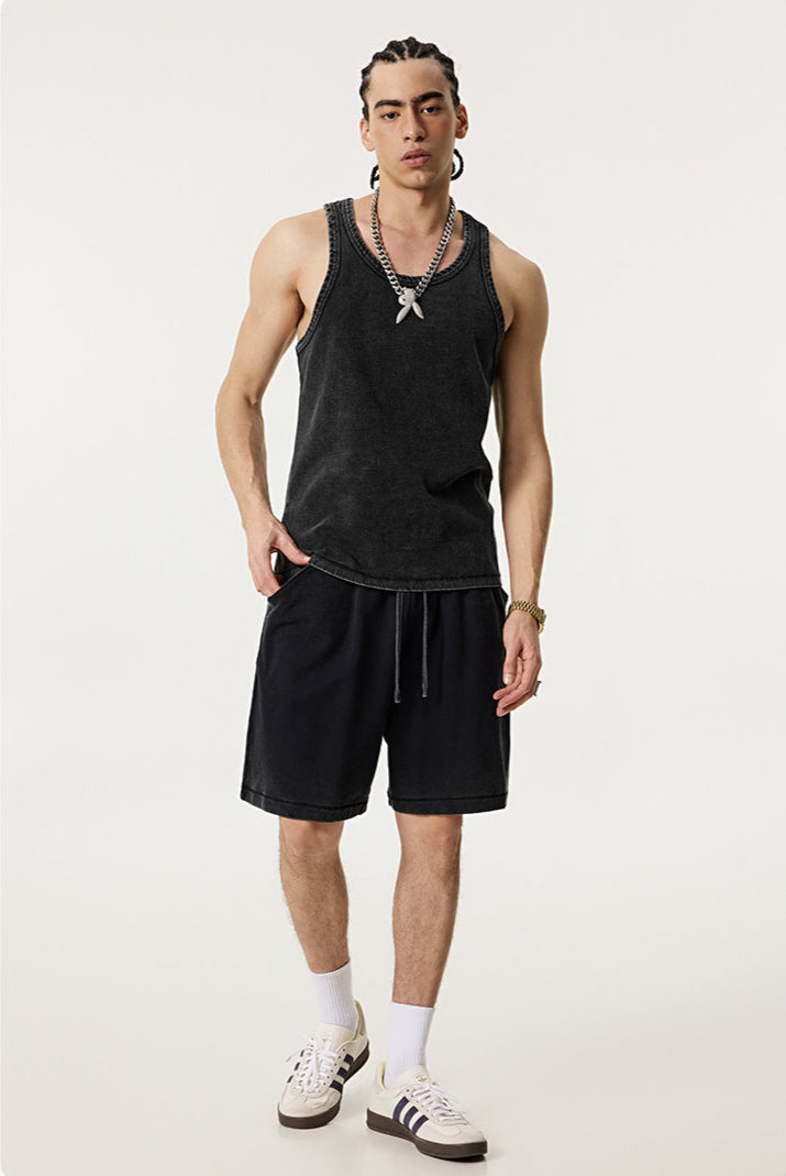 Male model casually posing in a washed black tank top and matching shorts, styled with silver accessories and sneakers