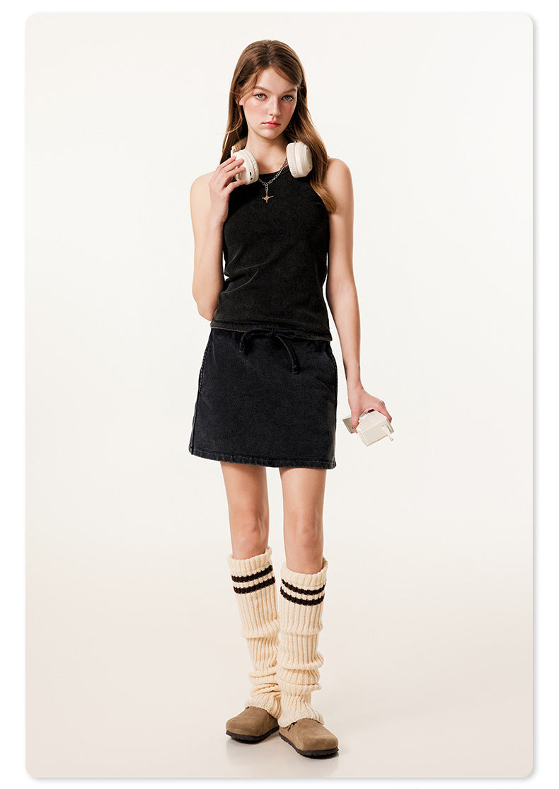 Full-length shot of model in all-black outfit with mini skirt, tank top, cream leg warmers and UGG-style boots