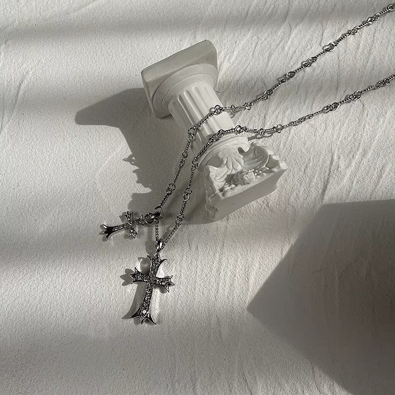 Silver cross pendant necklaces with crystal accents on delicate chain displayed on white fabric with decorative column