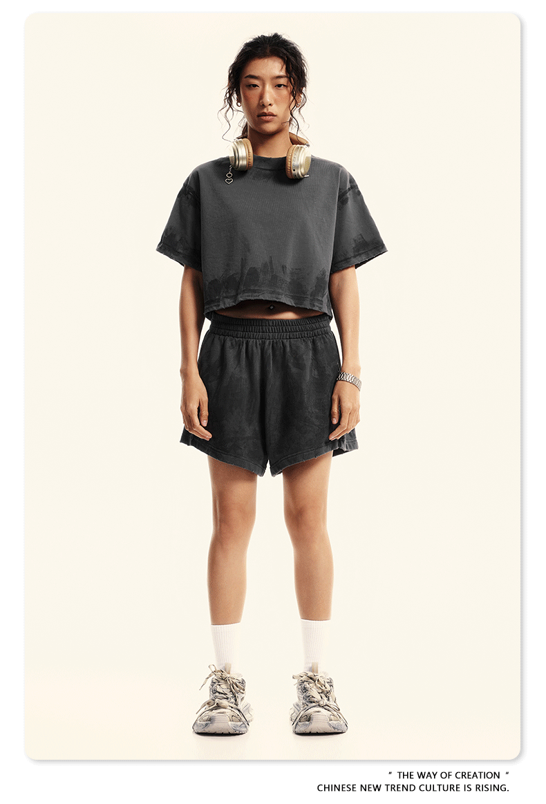Model in dark gray crop top and shorts set with headphones, white socks and chunky sneakers on beige backdrop