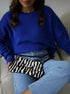 Royal blue sweater styled with zebra print handbag and light wash jeans, casual wear