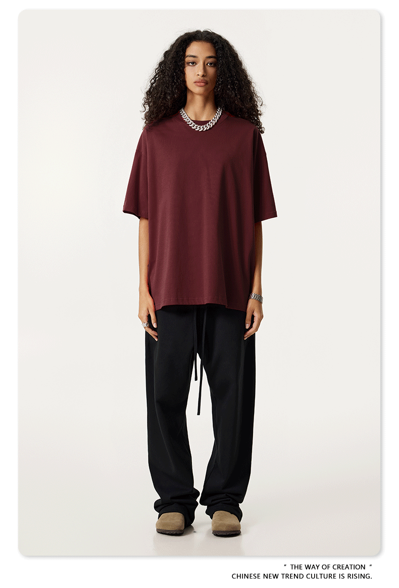 Female model with curly hair wearing burgundy oversized t-shirt, black drawstring pants and beige mules, styled with silver chain necklace