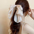 A woman with long brown hair wears a large champagne-colored sheer ribbon bow hair clip, styled in a half-up hairstyle.