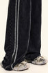 Bottom hem detail of black denim wide-leg pants showing ankle zipper closure with gray stripe trim and athletic footwearClose-up of elastic waistband with drawstring on black washed denim track pants featuring double gray side stripe detail