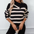 A woman is holding a coffee cup while modeling a black and white striped sweater with fold-over collar detail and gold jewelry accents