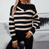A woman is posing with hand in pocket wearing a black and white striped knit sweater with asymmetrical collar and gold accent buttons