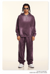 Model with twisted braids wearing purple sweatsuit with hoodie and wide-leg pants, styled with white sunglasses against cream background