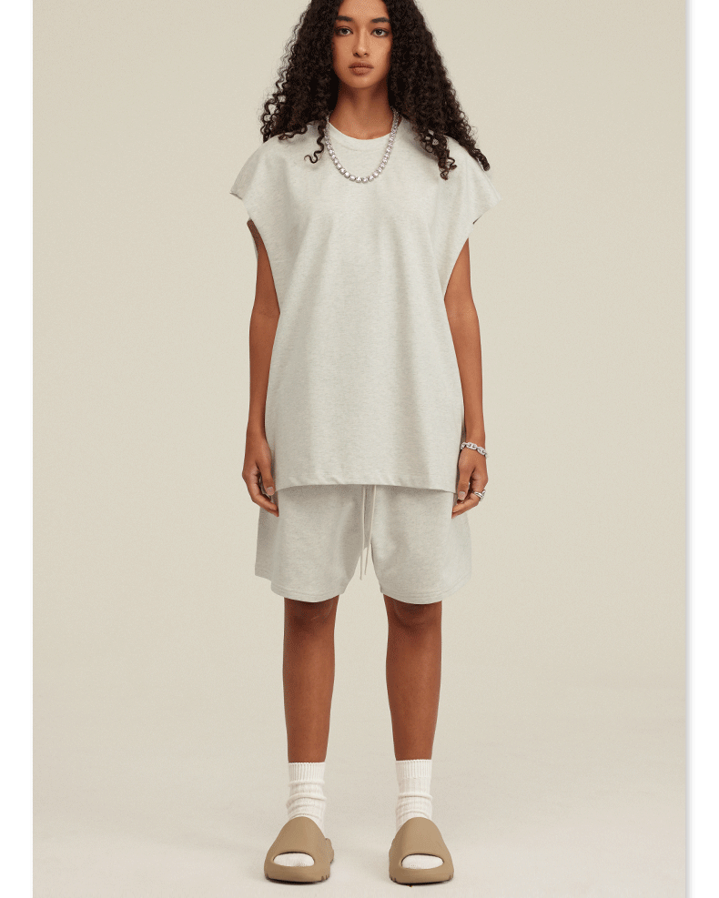 Model in white sleeveless top and matching shorts set with tan slides and silver chain necklace