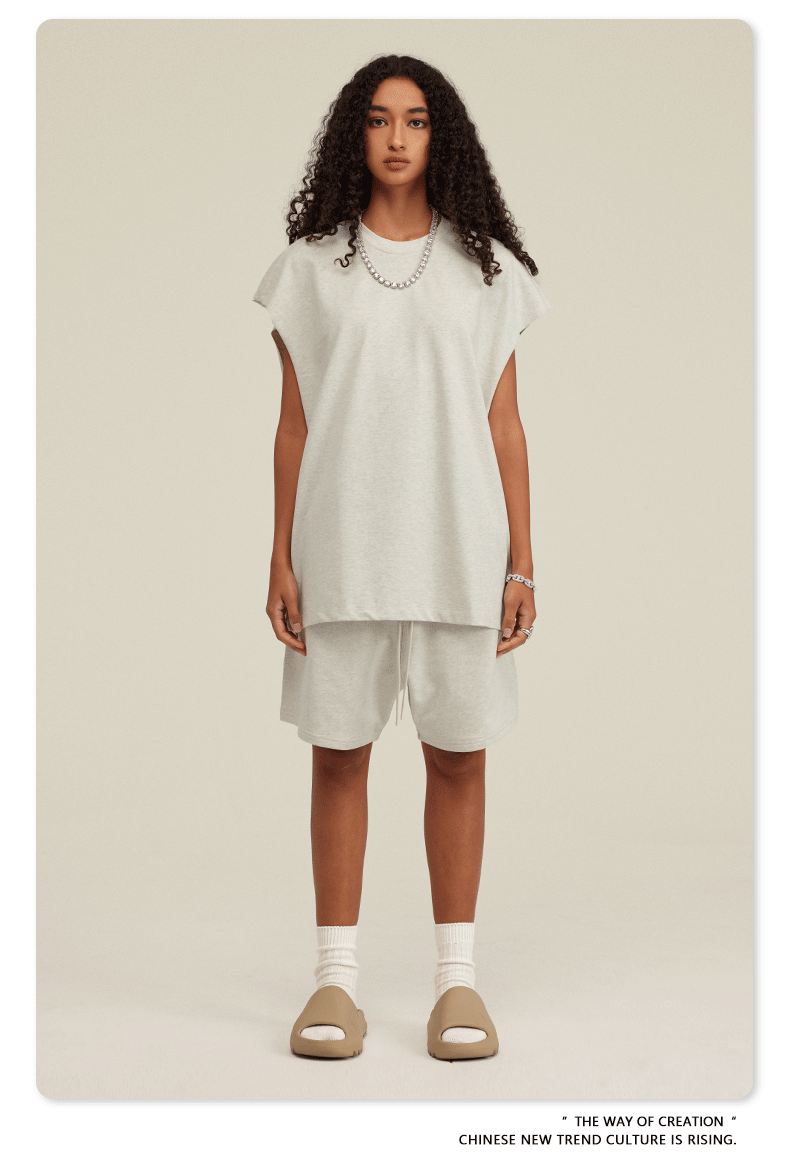 Model in white sleeveless top and matching shorts set with tan slides and silver chain necklace