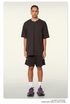 Model with braided hair wearing oversized black t-shirt and matching shorts with white socks and athletic shoes against cream background