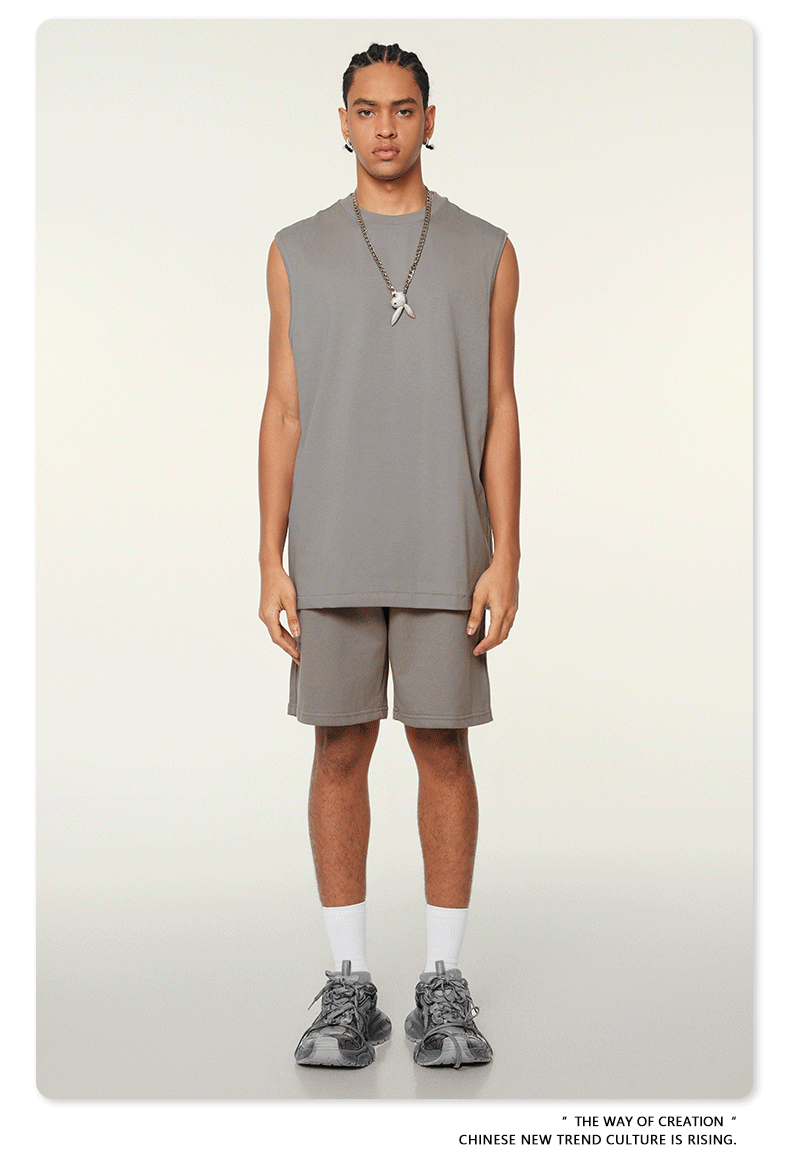 Model wearing gray matching set with oversized sleeveless top and shorts, silver pendant necklace and chunky white sneakers on neutral background