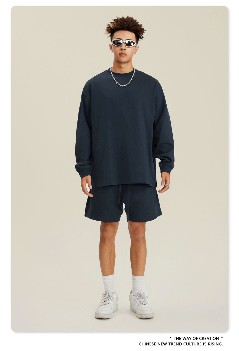 Man in navy sweatshirt and shorts set with white sunglasses, chain necklace and white sneakers