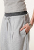 Detailed view of grey wide-leg sweatpants with a contrast waistband, drawstring, and side pocket, styled with a grey top.