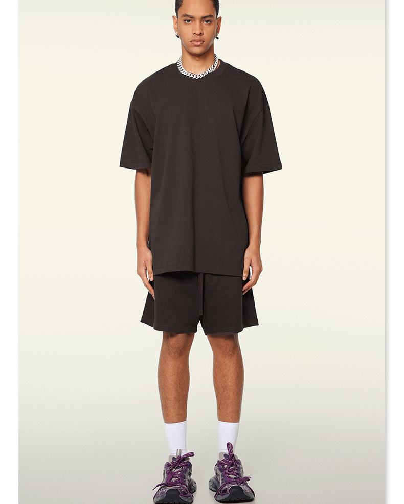 Model standing in black oversized t-shirt and matching shorts set with silver chain necklace and white socks with purple sneakers